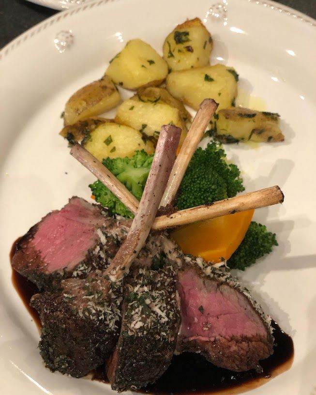 Herb-crusted rack of lamb chops, medium-rare, served with roasted baby potatoes, steamed broccoli and a carrot wedge on a white plate with balsamic glaze