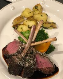 Herb-crusted rack of lamb chops, medium-rare, served with roasted baby potatoes, steamed broccoli and a carrot wedge on a white plate with balsamic glaze