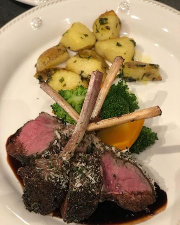 Herb-crusted rack of lamb chops, medium-rare, served with roasted baby potatoes, steamed broccoli and a carrot wedge on a white plate with balsamic glaze
