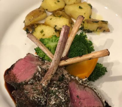 Herb-crusted rack of lamb chops, medium-rare, served with roasted baby potatoes, steamed broccoli and a carrot wedge on a white plate with balsamic glaze