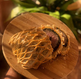 Sliced beef Wellington wrapped in lattice puff pastry with herb crust, revealing a medium-rare center on a round wooden cutting board