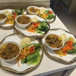 Four gold-rimmed plates on a kitchen counter, each with a bowl of hearty stew with potatoes, a swirl of mashed potatoes and a fresh side salad of lettuce, shredded carrots, corn and cherry tomatoes—restaurant-style plated comfort food.