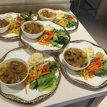 Four gold-rimmed plates on a kitchen counter, each with a bowl of hearty stew with potatoes, a swirl of mashed potatoes and a fresh side salad of lettuce, shredded carrots, corn and cherry tomatoes—restaurant-style plated comfort food.