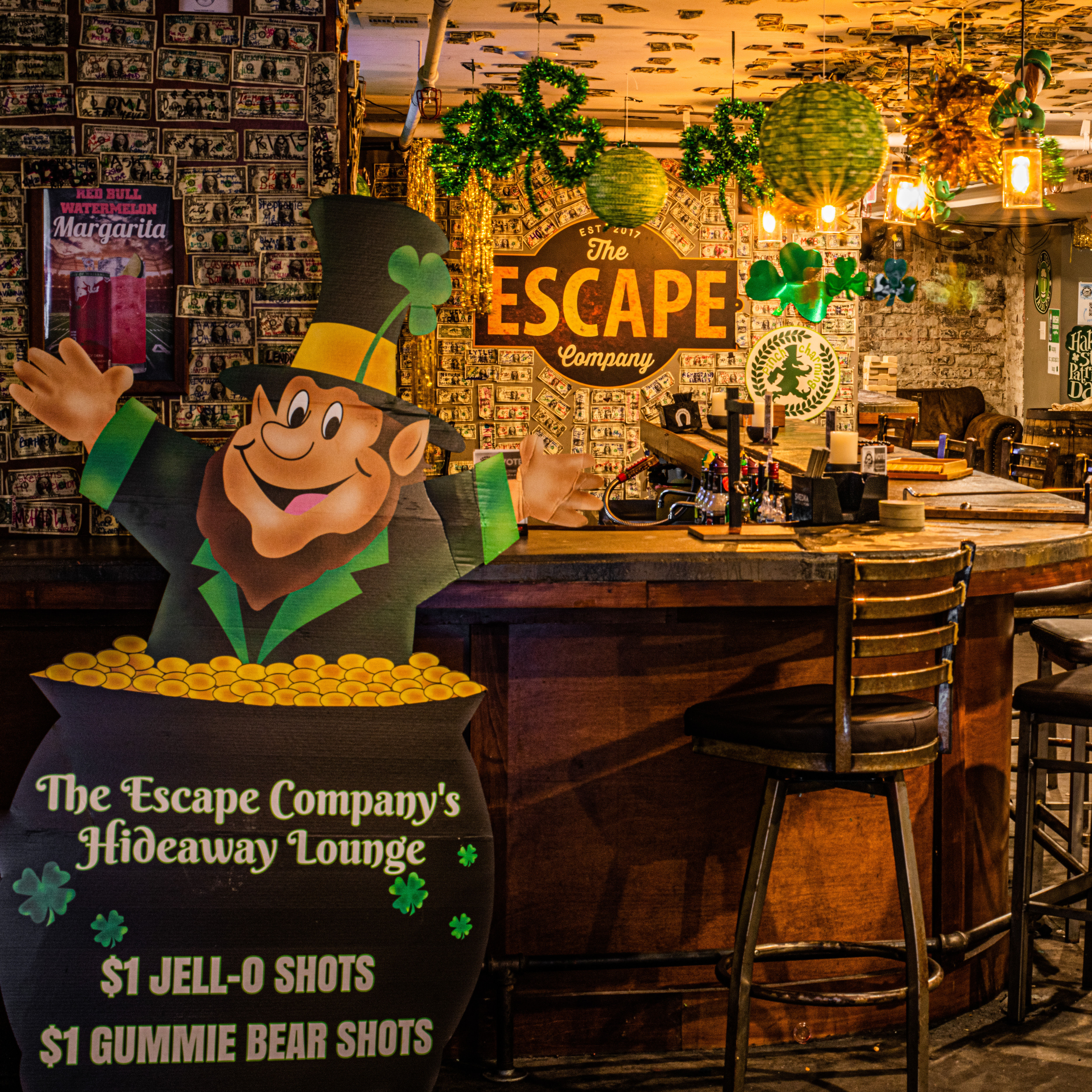 Cozy Irish-themed bar lounge with a cartoon leprechaun and pot of gold, shamrock decorations, dollar-bill–covered walls and wooden bar stools.