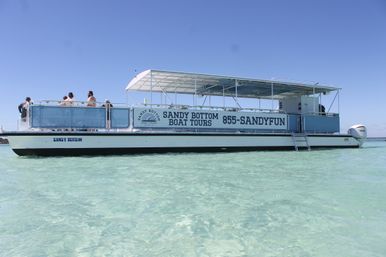 Open-air sightseeing boat anchored in crystal-clear shallow turquoise water under a bright blue sky, passengers on deck enjoying the view.