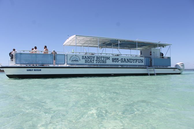 Open-air sightseeing boat anchored in crystal-clear shallow turquoise water under a bright blue sky, passengers on deck enjoying the view.