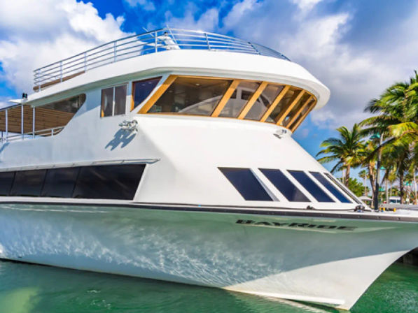 Sleek white luxury yacht docked in a tropical marina, bow and large windows reflecting turquoise water and a bright blue sky with palm trees