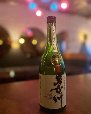 Green bottle of Japanese sake (nihonshu) with an award sticker on a bar countertop, warm bokeh string lights and cozy restaurant ambiance