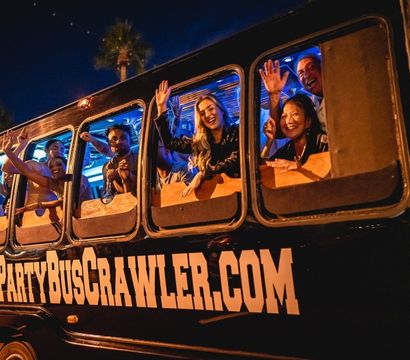 Happy group waving from windows of a nighttime Scottsdale party bus with colorful interior lights and palm trees, lively nightlife scene.