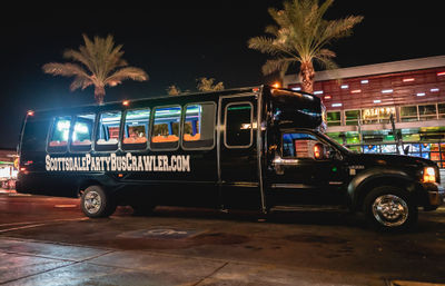 Black party bus with neon-lit interior parked under palm trees on a Scottsdale nightlife street at night