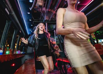 Two women dancing and laughing inside a neon-lit party bus at night, lively city nightlife vibe.