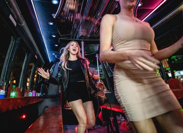 Two women dancing and laughing inside a neon-lit party bus at night, lively city nightlife vibe.