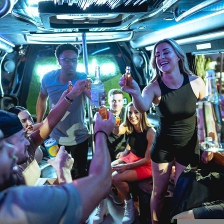 Group of friends cheering with shots and bottles inside a neon-lit party limo, upbeat nightlife celebration.