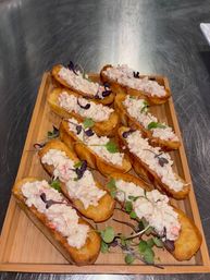 Mini lobster roll appetizers — chilled lobster salad piled on toasted brioche bites, garnished with microgreens on a wooden serving board
