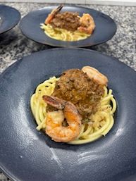 Plated shrimp spaghetti: nest of spaghetti topped with a large meatball and two sautéed shrimp on a matte black plate set on a granite countertop.