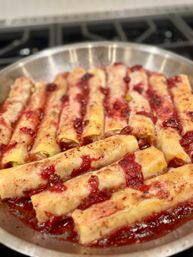 Golden baked cannelloni-style pasta rolls filled with cheese, topped with chunky red tomato sauce in a round metal skillet on a stovetop