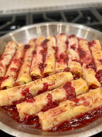 Golden baked cannelloni-style pasta rolls filled with cheese, topped with chunky red tomato sauce in a round metal skillet on a stovetop