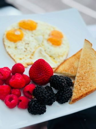 Colorful breakfast plate with sunny-side-up eggs, triangular toasted bread and fresh berries (strawberry, raspberries, blackberries) on a white plate