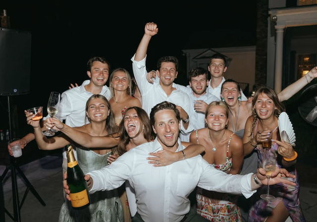 Group of smiling young adults cheering with glasses and a champagne bottle at an outdoor nighttime patio celebration