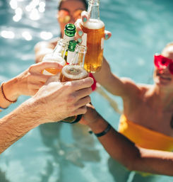 Clinking beer bottles in a sunny pool — summer pool party with friends, swim and cheers