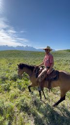 Cowboy on horseback crossing sagebrush prairie with distant jagged mountain peaks under a wide blue sky