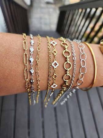 Stacked gold and silver delicate chain bracelets and thin bangle on a wrist, outdoor wooden deck background