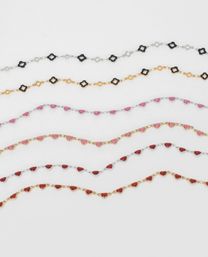 Flatlay of dainty gold and silver chain bracelets featuring glittery pink and red heart charms and black quatrefoil links on a white background