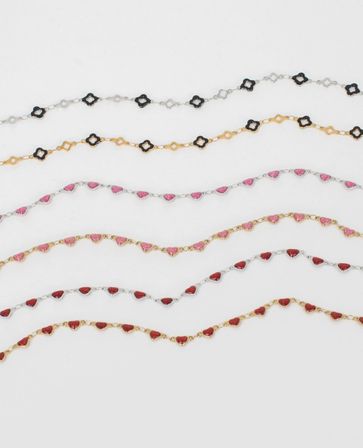 Flatlay of dainty gold and silver chain bracelets featuring glittery pink and red heart charms and black quatrefoil links on a white background