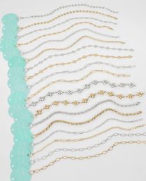 Flat-lay of gold and silver delicate chain bracelets in assorted link styles, arranged in parallel rows on a white background with teal circular product tags