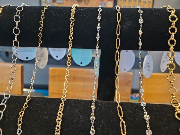Close-up of a retail jewelry display on a black velvet rack featuring assorted gold and silver chain necklaces with varied link styles and small bead accents.