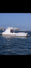 White pontoon party boat carrying a small group of people cruising coastal waters past beachfront condominiums under a clear blue sky
