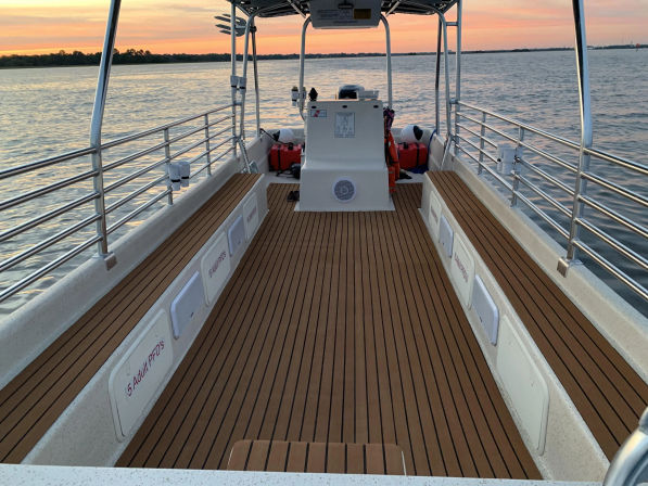 Sunset-lit open boat deck with faux teak planks, polished stainless railings and center console heading out over calm coastal waters.