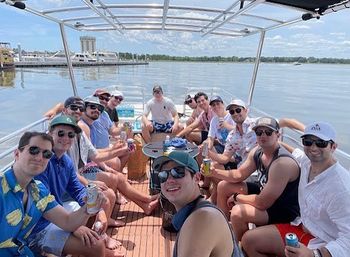 Cheerful group on a pontoon boat enjoying a sunny summer day on a calm river with a waterfront city skyline in the distance