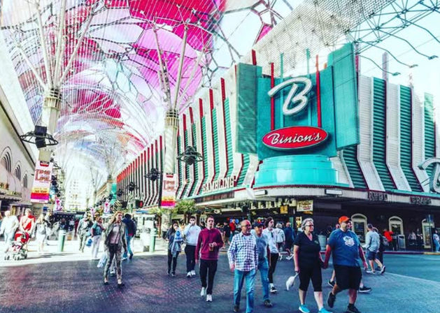 Vibrant crowds strolling under a colorful LED canopy in downtown Las Vegas past a retro turquoise casino marquee