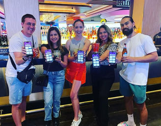 Group of five friends at a lively casino-style bar holding cocktails and smartphones displaying an app, smiling for a night out.