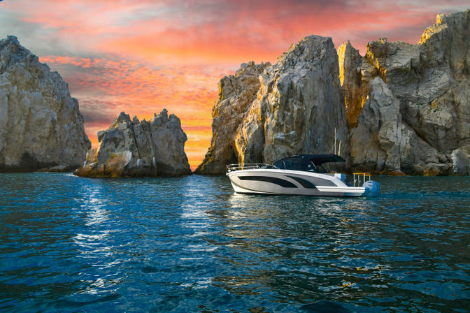 Sleek motorboat floating beside dramatic rocky sea cliffs at sunset, fiery sky reflected on turquoise ocean water.