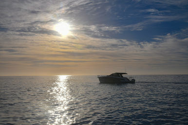 Motorboat silhouetted on calm ocean at sunset with sun reflecting on rippled water and streaked clouds