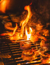 Flame-kissed shrimp sizzling on a charcoal grill over open flames, golden-seared and smoky — backyard seafood barbecue.