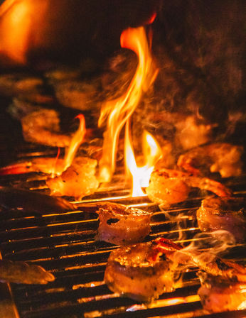 Flame-kissed shrimp sizzling on a charcoal grill over open flames, golden-seared and smoky — backyard seafood barbecue.