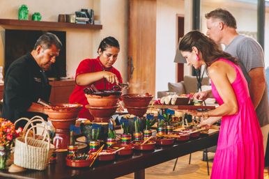 Indoor Mexican-style taco bar with guests serving tacos from stacked clay pots and molcajetes — steaming mole, colorful salsas, tortillas and condiments on a buffet table.