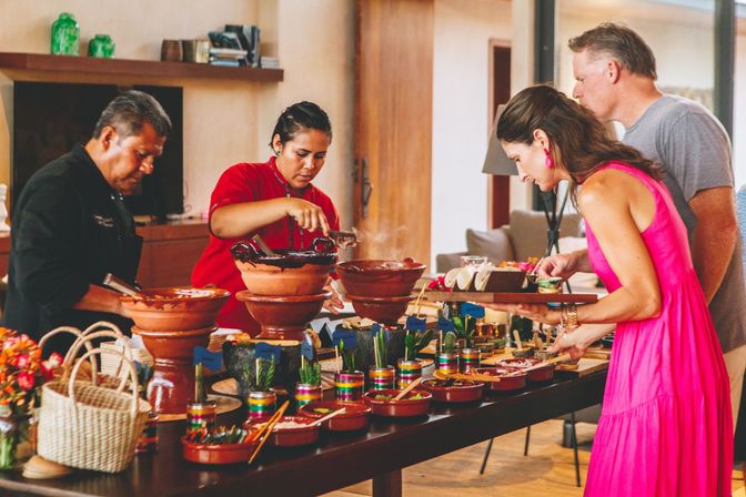Indoor Mexican-style taco bar with guests serving tacos from stacked clay pots and molcajetes — steaming mole, colorful salsas, tortillas and condiments on a buffet table.