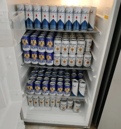 Upright refrigerator stocked with neat rows of Michelob Ultra, Tecate, and Corona Light beer cans on metal shelves, ready for chilling