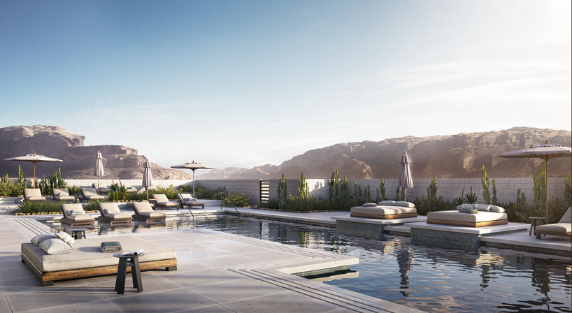 Luxury outdoor pool at a modern desert oasis with plush daybeds, sun loungers and umbrellas beside reflective water, framed by rocky canyon cliffs under soft sunlight.