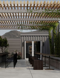 Modern outdoor patio with wooden slatted pergola and climbing vines, long bar counter with black stools, cube seats and round bistro tables in front of a corrugated metal building with mountain backdrop.