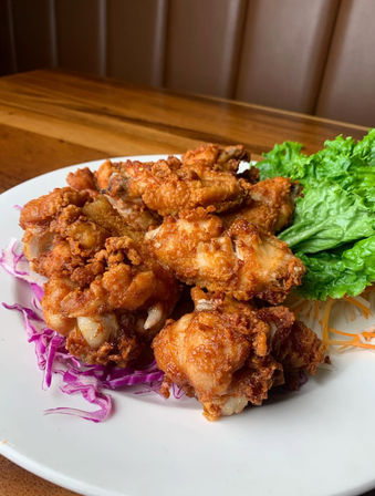 Crispy golden fried chicken wings piled on a white plate with shredded purple cabbage and fresh green lettuce on a wooden restaurant table