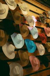 Playful display of colorful cowboy hats mounted on a wooden slat wall — pastel pink, sky blue, tan, white and camo styles in a western retail setting.