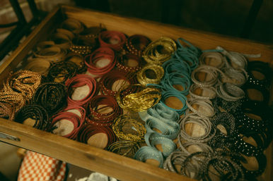 Neatly arranged colorful bangles and bracelets — braided, studded, leather and metallic cuffs rolled into rows inside a wooden drawer.