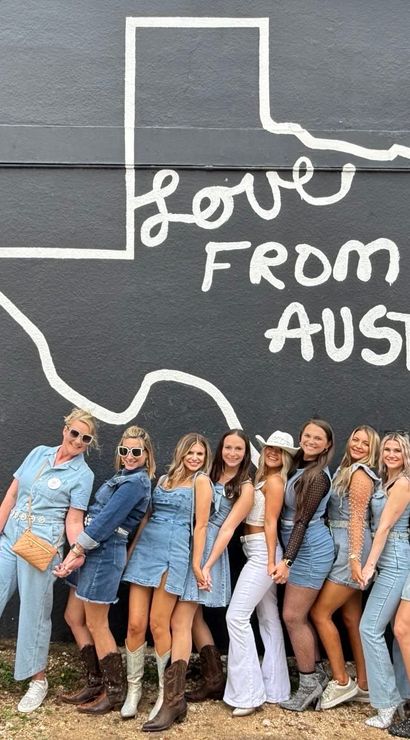 Smiling group of women in denim outfits and cowboy boots posing in front of a black mural of the Texas outline that reads "Love From Austin" — popular Austin, Texas photo spot.