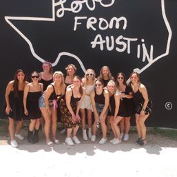 Smiling group of women in summer outfits posing on a sunny sidewalk in front of a bold black-and-white “Love From Austin” Texas mural.