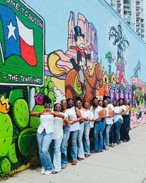 Line of women in white tops and jeans wearing round sunglasses, posing in front of a vibrant Austin, Texas street-art mural with a Lone Star flag and cartoon cowboy on horseback.